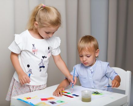 The boy and girl, brother and sister paint watercolors at the table on white sheets of paper. Concept aesthetic development of children, happy childhood.