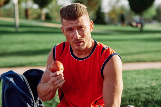 man in the park sits on a bench and eats an apple summer. High quality photo