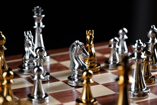 Gold and silver chess figures placed on wooden chessboard. Intellectual duel and tactical battle in business. Strategy planning, leadership and teamwork concept. Close-up metal chess pieces on board.