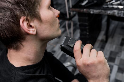 A guy with dark hair shaves with an automatic razor. Care for your appearance.