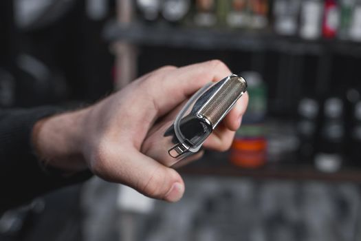 The hand of a barber or hairdresser holds an automatic clipper for cutting and shaving close-up against the background of the salon.