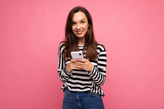 Photo of a shocked positive emotional surprised young woman posing isolated over pink wall background using mobile phone