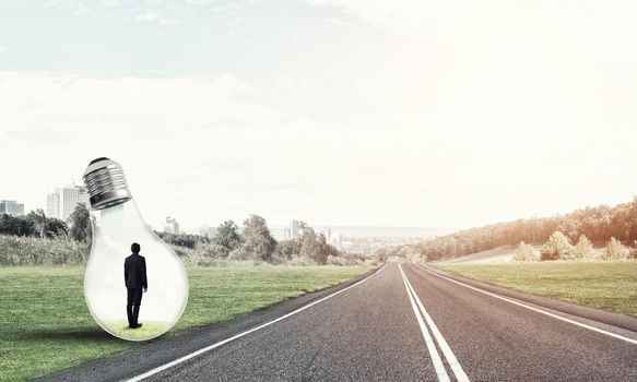 Young businessman trapped inside of light bulb on asphalt road