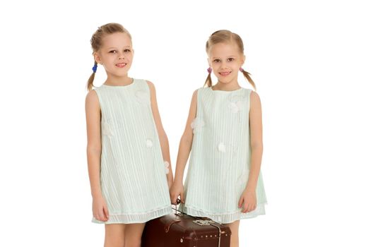 Two lovely little girls in short summer blue dresses , carrying a large , old grandma suitcase - Isolated on white background