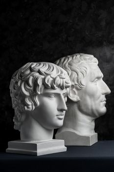 White gypsum copy of ancient statue of Guy Julius Caesar Octavian Augustus and Antinous head for artists on a dark textured background. Plaster sculpture of mans face.