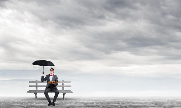 young student with umbrella and book sits on a bench