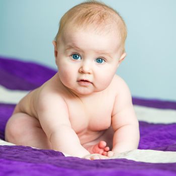 blue-eyed baby sitting on the bed