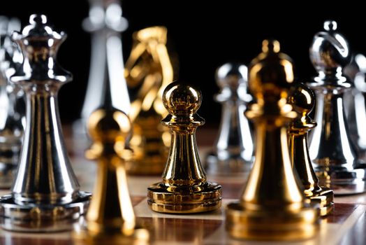 Gold and silver chess figures placed on wooden chessboard. Intellectual duel and tactical battle in business. Strategy planning, leadership and teamwork concept. Close-up metal chess pieces on board.