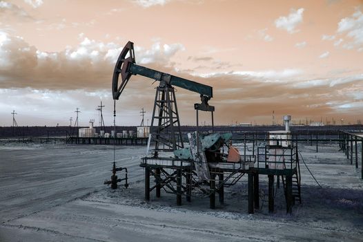 Oil pump jack and wellhead with valve armature during sunset on the oilfield. Extraction of oil. Oil and gas concept. Toned.