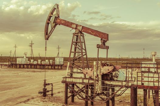 Oil pump jack on a oil field. Cloudy sky background. Extraction of oil. Petroleum concept. Toned.