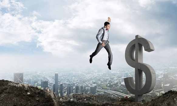 Jumping businessman in smart casual wear crashing big dollar symbol with city view on background.