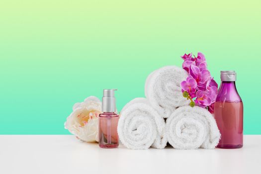 Stack of white towels and bottles of skincare on white table, front view