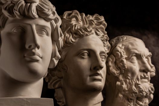 Group gypsum busts of ancient statues human heads for artists on a dark background. Plaster sculptures of antique people faces. Renaissance epoch style. Blank for creativity. Academic subject.
