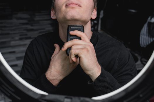 A guy shaves with an automatic razor next to the ring lighting. Care for your appearance.