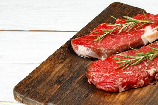 Barbecue veal steaks with rosemary on wooden board. Raw meat