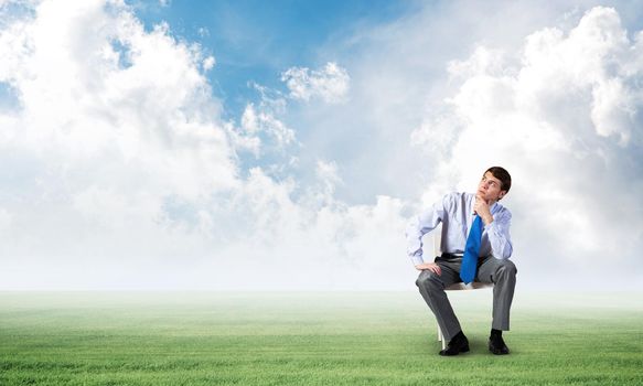 young businessman sits on an office chair, thoughtful and looking up