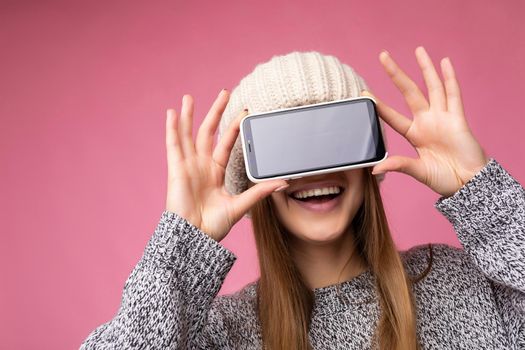 Photo of beautiful smiling young woman good looking wearing casual stylish outfit standing isolated on background with copy space holding smartphone showing phone in hand with empty screen display for mockup.