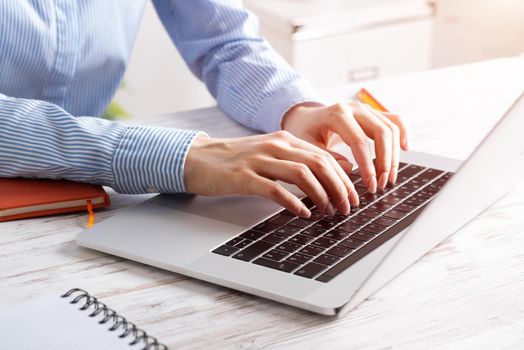 Close up business woman hands typing at laptop keyboard. Side view office workplace with computer on white wooden table. Professional business occupation design with secretary working at desk.