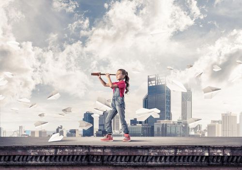 Cute kid girl standing on house roof and looking in spyglass