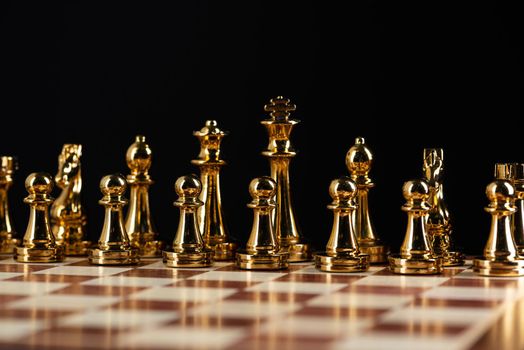 Golden chess figures standing on chessboard. Intellectual competition and fight in business. Strategy planning and leadership concept with copy space. Gold chess pieces in row on black background.