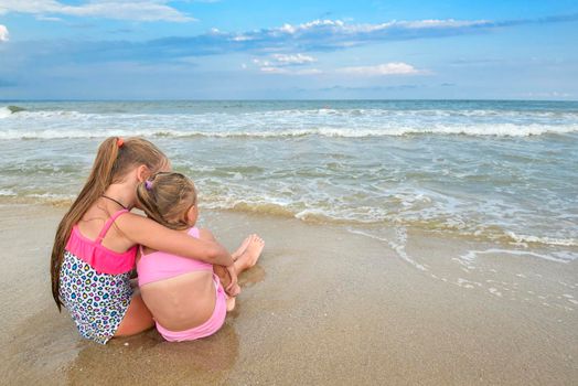 Two girls sitting on the beach and looking at the evening sea. Children on the sea beach and beautiful skyline.