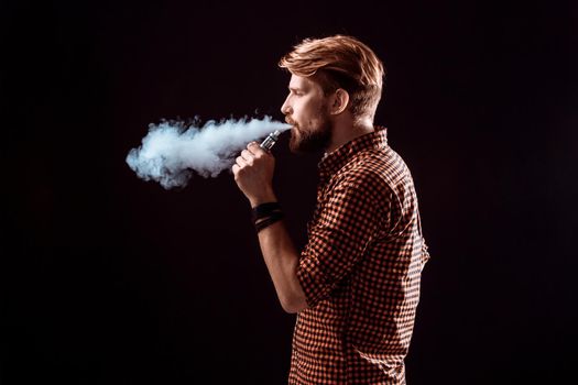 young man wearing a plaid shirt smokes an electronic cigarette on a black background