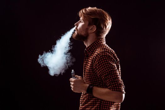 young man wearing a plaid shirt smokes an electronic cigarette on a black background