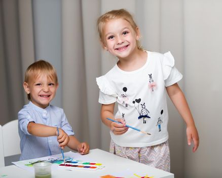 The boy and girl, brother and sister paint watercolors at the table on white sheets of paper. Concept aesthetic development of children, happy childhood.