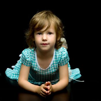 Charming little girl is lying on the studio floor on a black background. Concept for happy childhood, style and fashion