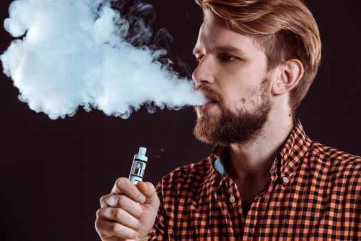 young man wearing a plaid shirt smokes an electronic cigarette on a black background