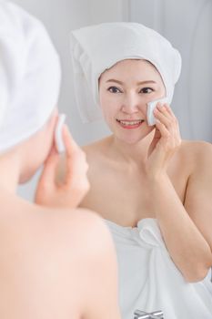 Beautiful woman looking mirror and cleaning her face with cotton