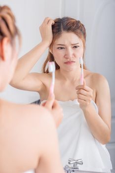 unhappy woman in bath towel brushing teeth with mirror in the bathroom