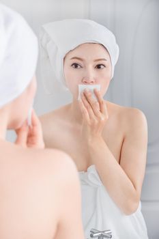 Beautiful woman looking mirror and cleaning her face with cotton