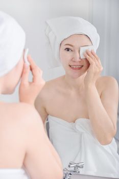 Beautiful woman looking mirror and cleaning her face with cotton