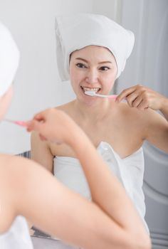 woman in bath towel brushing teeth with mirror in the bathroom