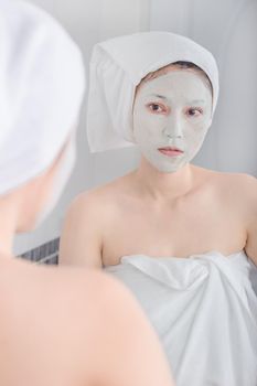 woman applying mask on her face and looking in the mirror in the bathroom