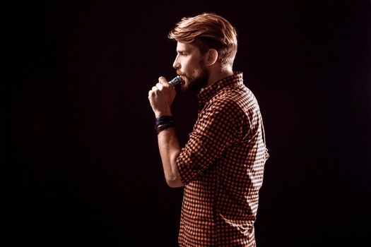 young man wearing a plaid shirt smokes an electronic cigarette on a black background