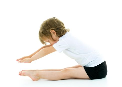 Cute little girl performs gymnastic exercises on the floor in the studio on a white background. The concept of sports, the physical development of children