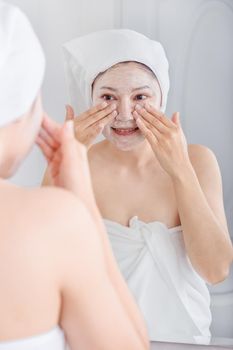 woman applying mask on her face and looking in the mirror in the bathroom