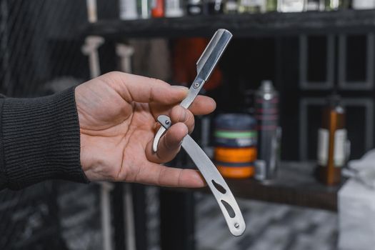 The hand of a barber or professional hairdresser holds a straight tool sharp razor equipment for shaving and beard care, close-up.
