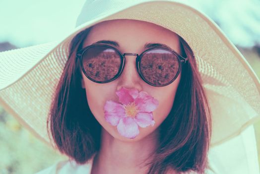 Portrait of young woman in sunglasses and hat with wide brim with flower, concept of summer mood. Fashionable and beautiful summer girl. Image with instagram color effect