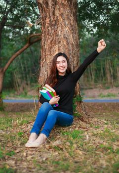 cheerful woman  holding a book with arm raised in the park