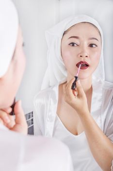 woman looking in the mirror and applying red lipstick on her lips