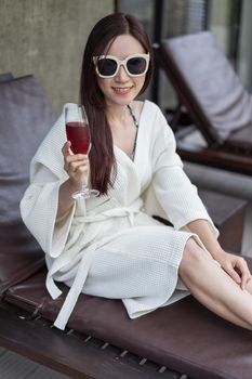 woman clothed bathrobe sitting on deckchair in swimming pool