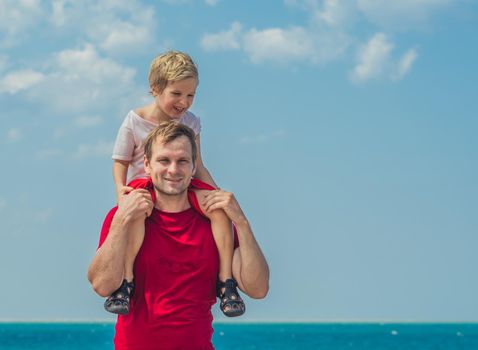 Happy smile father hugs holds on shoulders boy male child stand blue lazur sea panorama skyline horizon sunshine day clear sky. Travel, relationship, dad responsibilities, influence on son worldview.