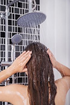 woman is washing her hair and face by rain shower head, rear view