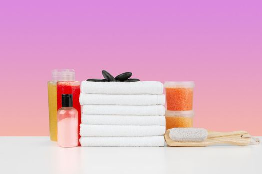 Stack of white towels and bottles of skincare on white table, front view