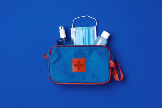 First aid kit with mask and sanitizer on blue background close up