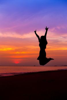 Silhouette of woman jumping with hands up and showing I LOVE YOU sign on the sea beach at sunset