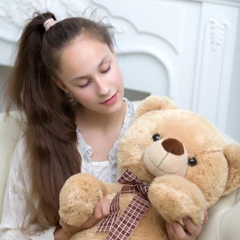 Beautiful little girl schoolgirl embraces with a teddy bear. The concept of a happy childhood, children's emotions.